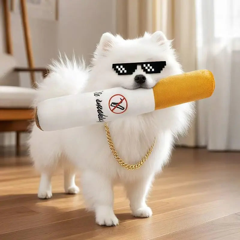 A fluffy white dog holds a yellow cigar-shaped toy with black sunglasses and a prohibition symbol on it.