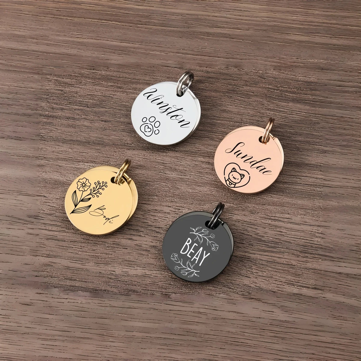 Three personalized stainless steel pet ID tags engraved with names Winston Sundae and Beay resting on a wooden surface.
