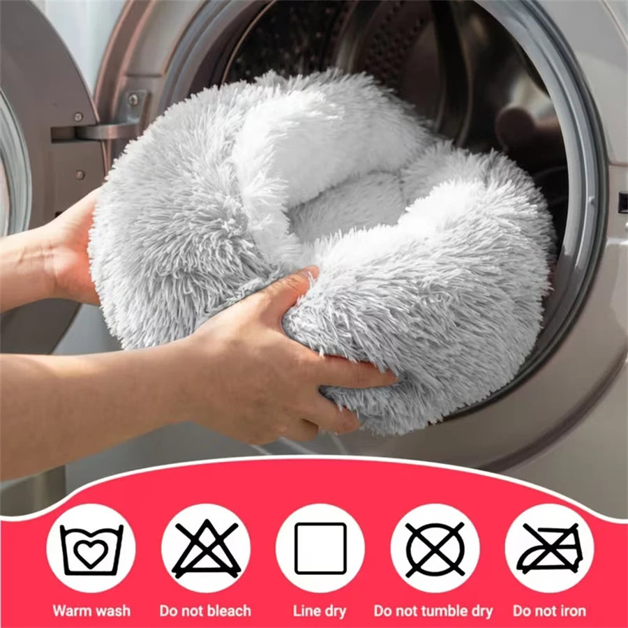 Hands are placing a plush gray pet bed nest inside a washing machine drum.