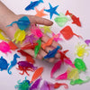 A hand holds a colorful set of ten soft rubber goldfish bath toys in various bright colors.