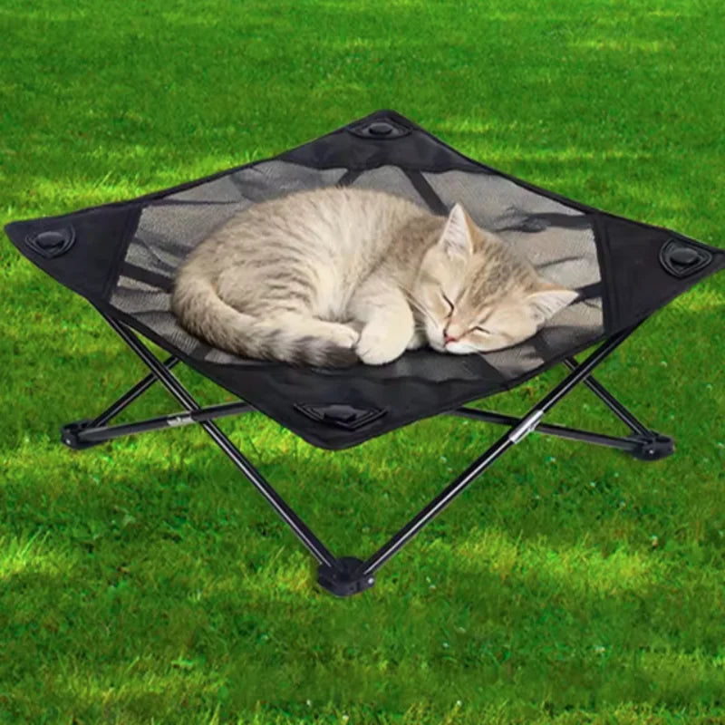 A light gray cat is relaxing in a black foldable elevated pet cot with breathable mesh on a green lawn.