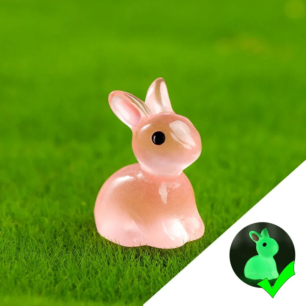A pink resin bunny figurine with a black eye sitting on bright green grass.