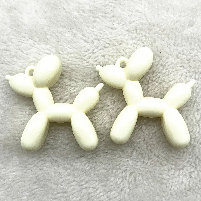 A pair of white acrylic balloon dog charm pendants lying on a light gray fuzzy surface.