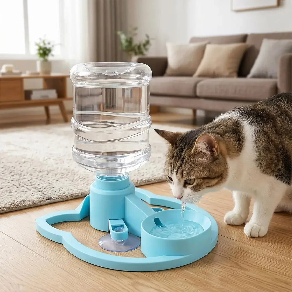 A blue gravity cat water dispenser with a bowl is positioned on the floor near a cat drinking from it.