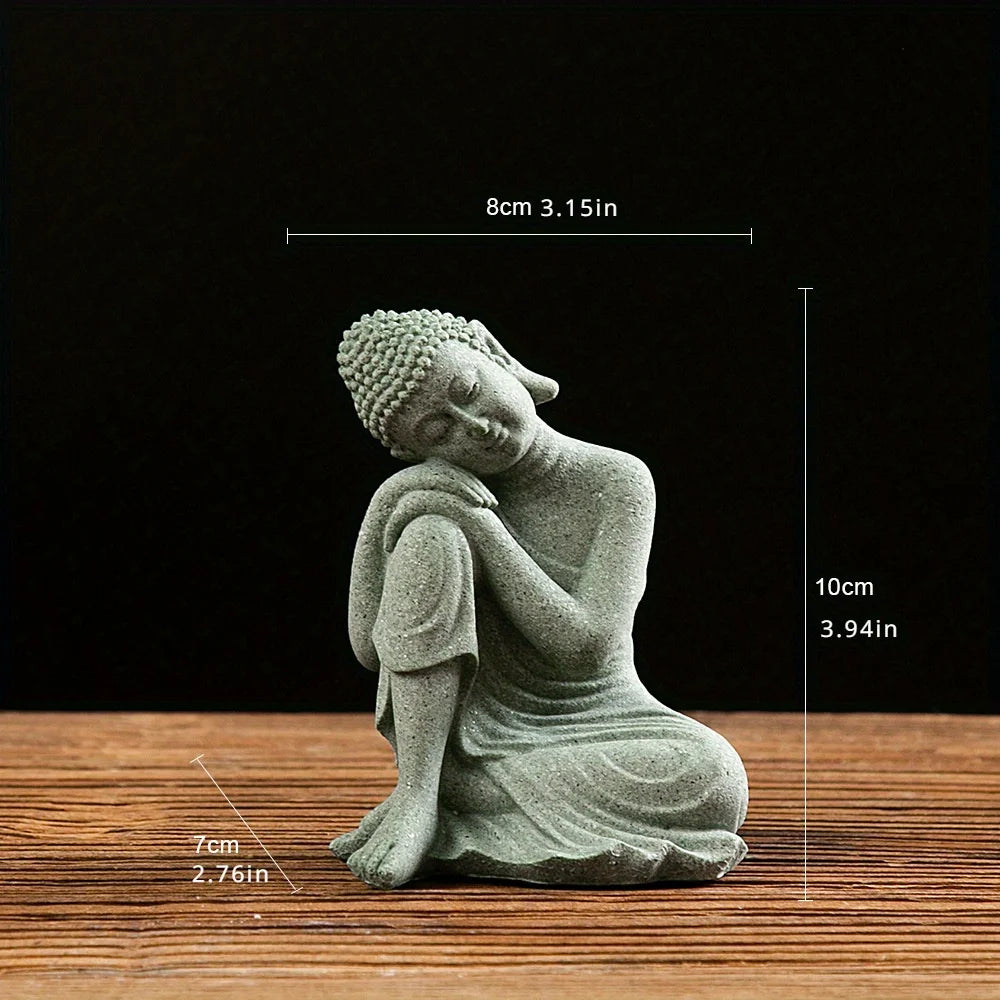 A small, grey stone statue of the Buddha in a meditative pose, resting on a wooden surface.