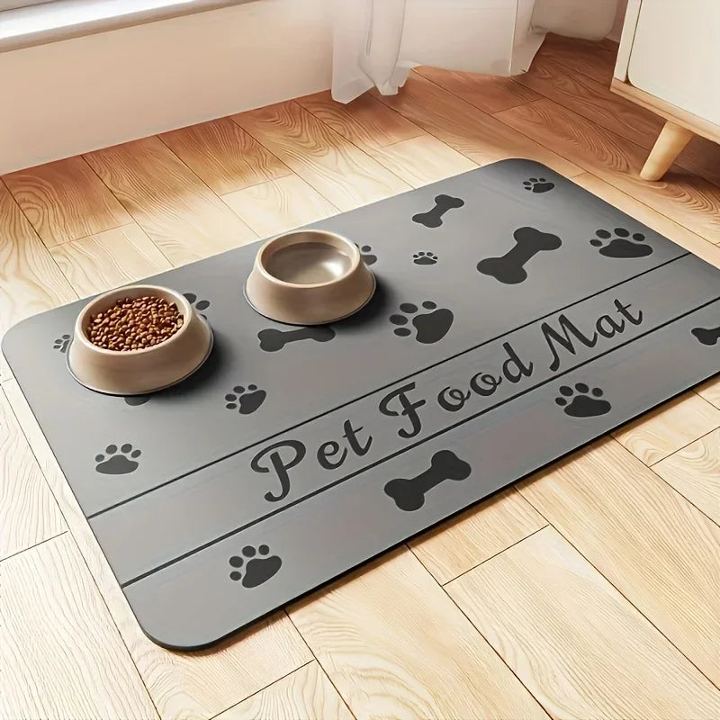 A gray pet food mat with paw prints and a bone shape is placed on a wooden floor next to a bowl of pet food.