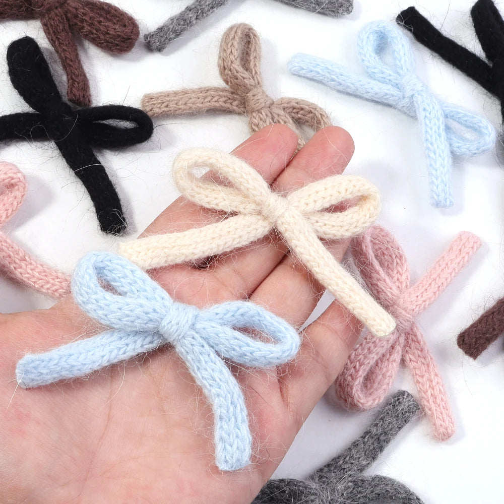 A hand holds a set of six handmade knitted cotton bows in various pastel and neutral colors for crafting.