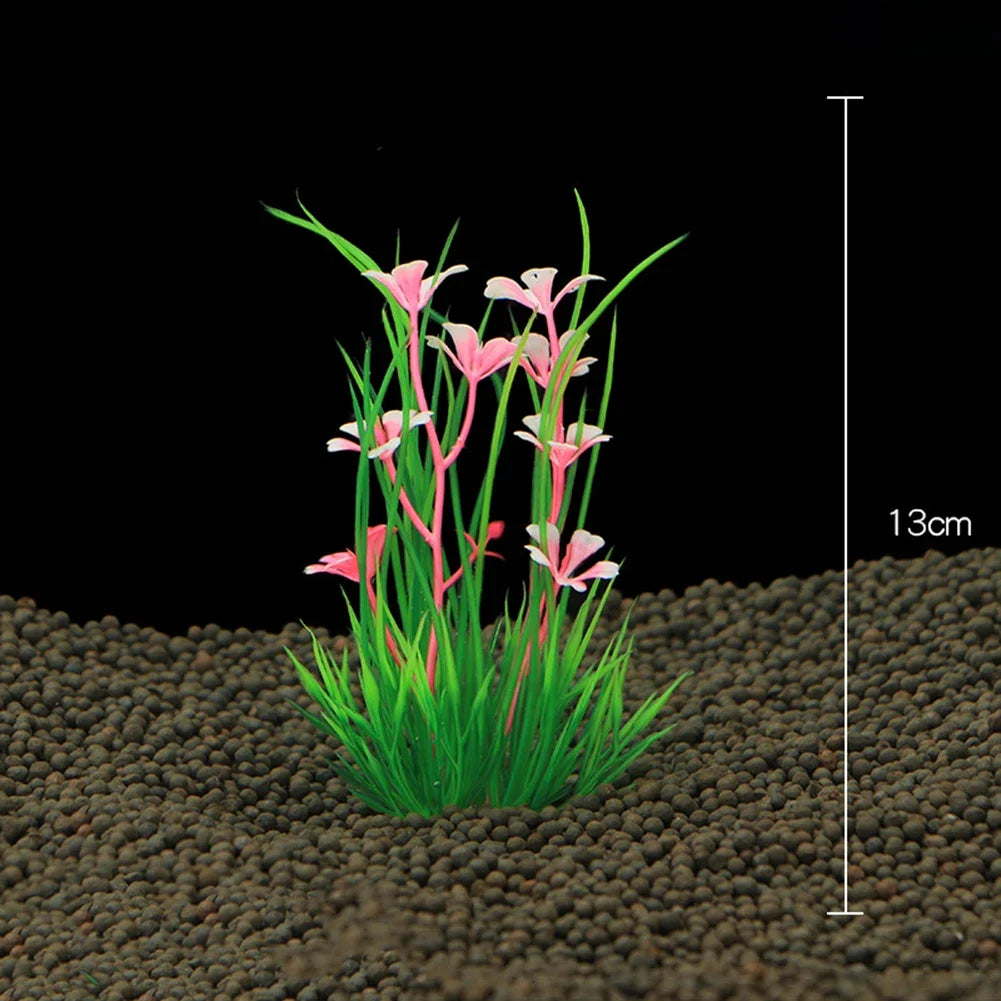 A cluster of pink and green artificial aquarium plants growing in dark substrate with a scale marker.