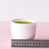 A white bowl filled with bright green artificial plant material, measured against a ruler.