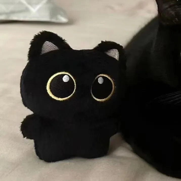 A small, black cat plush pendant with large gold eyes resting on a light surface.