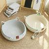 A woven cat scratcher and comfort bed with play balls resting on a jute rug next to wooden furniture.