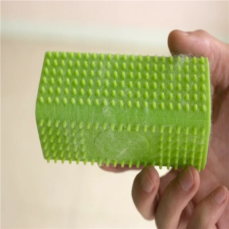 A hand holds a bright green silicone pet hair remover brush with textured bristles.