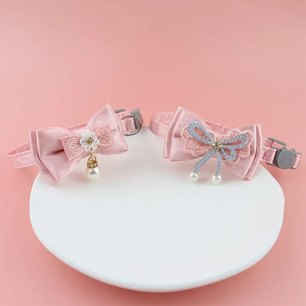 Pink lace bow cat collar with a pearl bell and bead charm displayed on a white background.