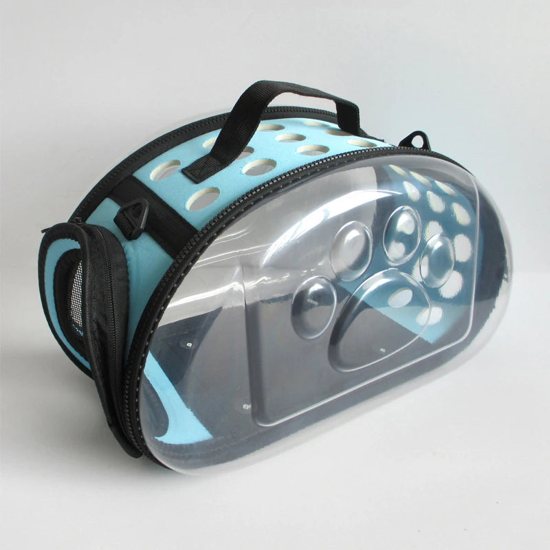 A transparent foldable pet travel carrier with a black shoulder strap and light blue accents.