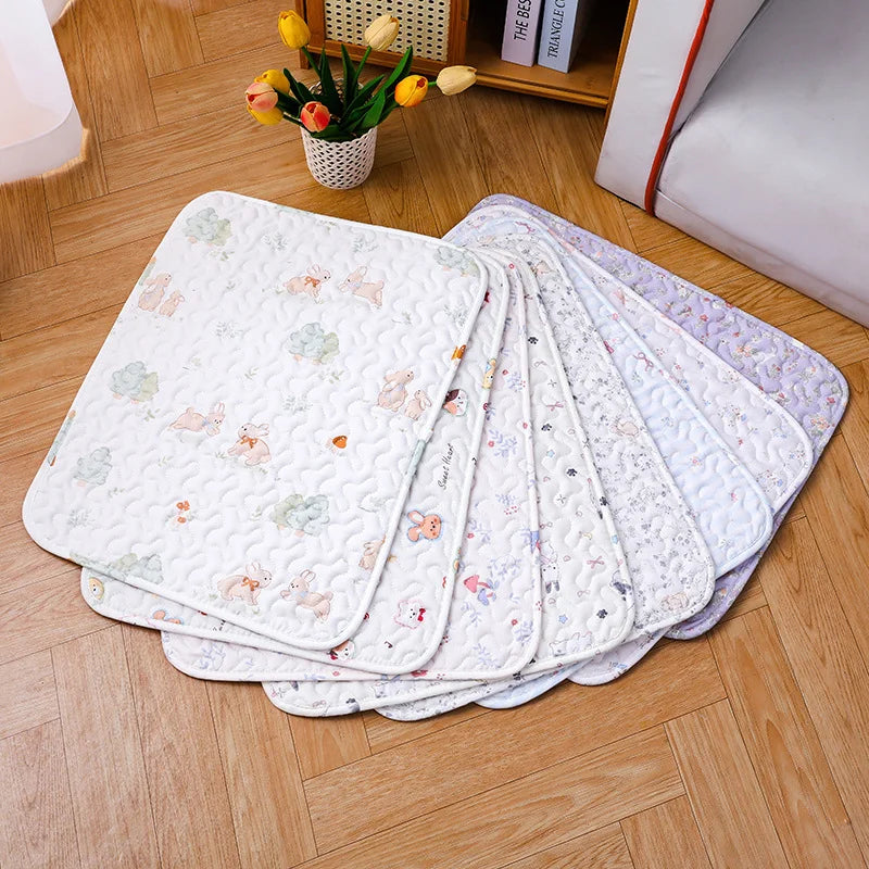A stack of soft cotton pet cage mats with various floral and animal patterns on a wooden floor.