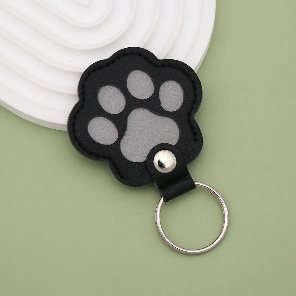 A black leather pet paw print charm with a gray paw pad and a silver keyring.