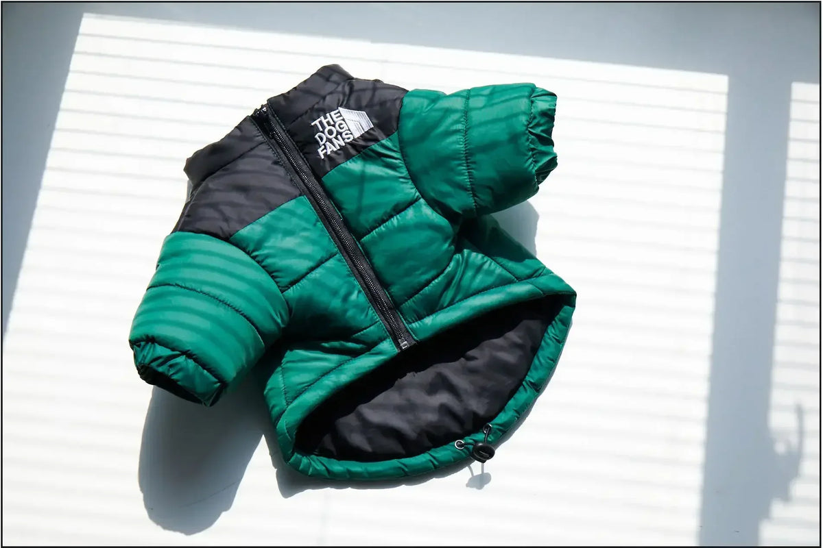 A dark green and black quilted coat for a dog, shown flat against a white slatted surface.