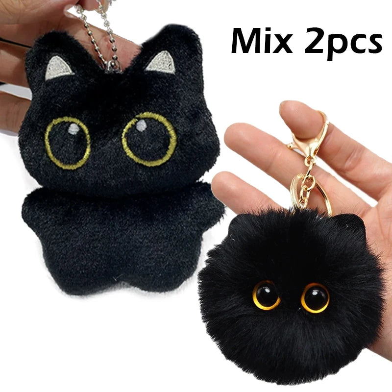 A black cat plush pendant with gold-colored eyes is shown being held by a hand.