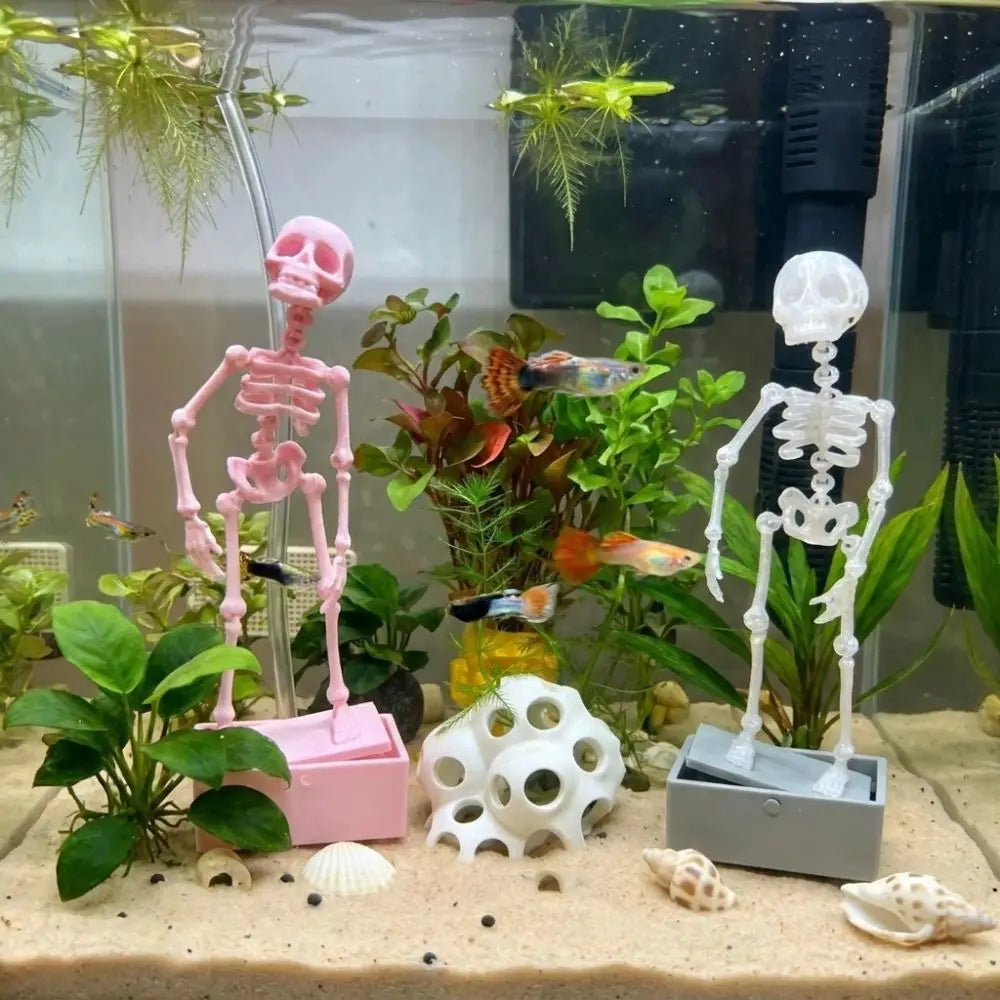 A pink dancing skeleton figure is displayed in a glass aquarium with various plants and sea shells.