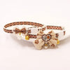 A beige breakaway cat collar featuring a patterned strap, a bowknot, and a small bell.