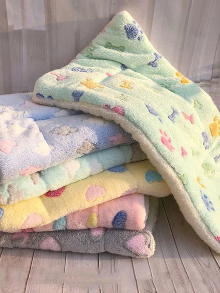 A stack of colorful plush fleece blankets and mats for pets, including light green, yellow, pink, and blue shades.