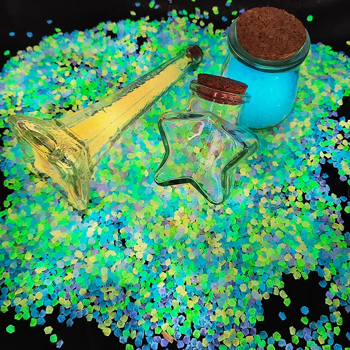 A glass bottle with a cork and a clear star-shaped object rests on a bed of brightly colored glow-in-the-dark resin pebbles.