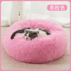 A fluffy pink round pet bed with a white and gray kitten resting inside.