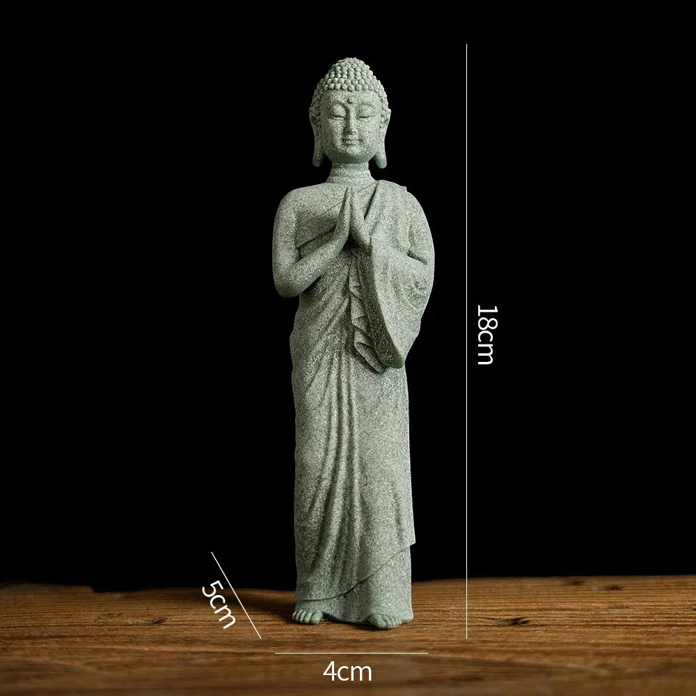 A small, light gray Buddha stone statue with hands pressed together, standing on a wooden surface.