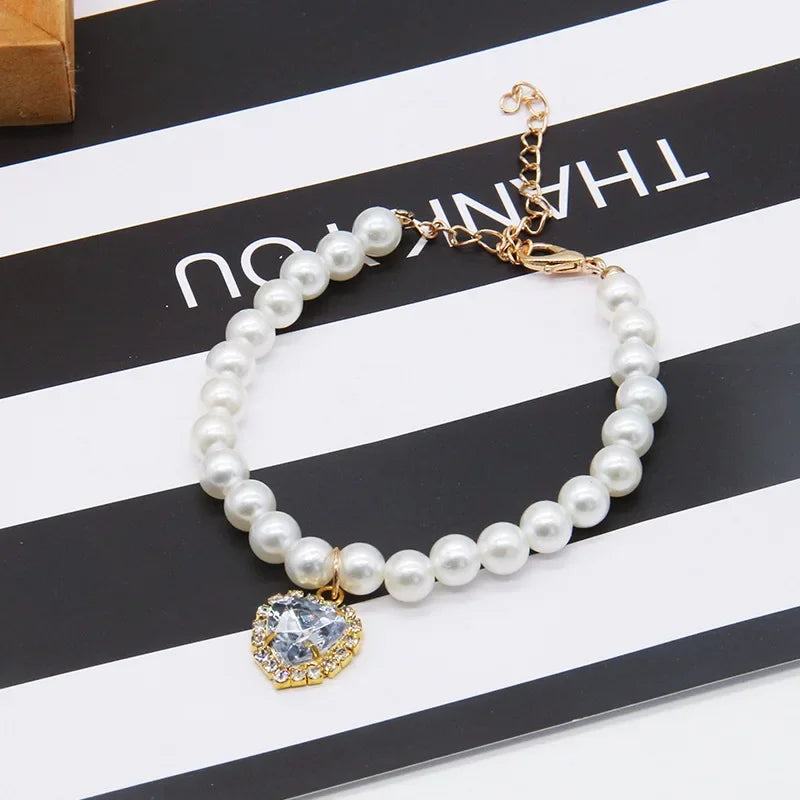 A pearl necklace with a gold-toned pendant is displayed on a black and white striped background.