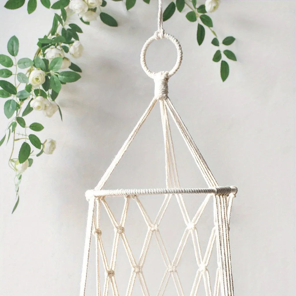 A white macrame cat hammock bed hanging from a hook, decorated with green leaves.