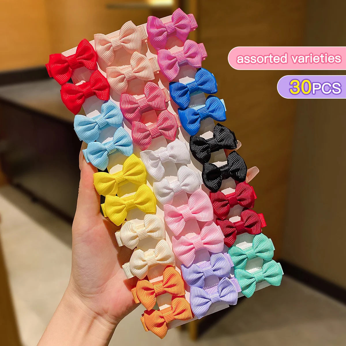 A hand holds a variety of assorted pink, red, blue, and yellow fabric hair clips in a display box.