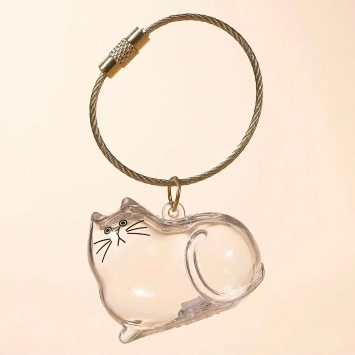 A clear glass charm shaped like a cat is attached to a braided gold-colored keychain ring.