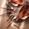 A collection of six wooden tea and coffee spoons arranged on a woven mat and wooden surface.