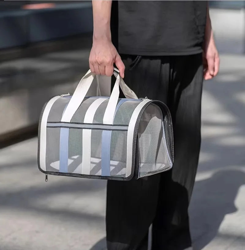 A person holds a gray and white mesh foldable travel carrier bag for pets.