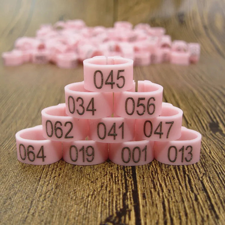 A stack of pink plastic bird identification foot rings with various numerical markings on a wooden surface.