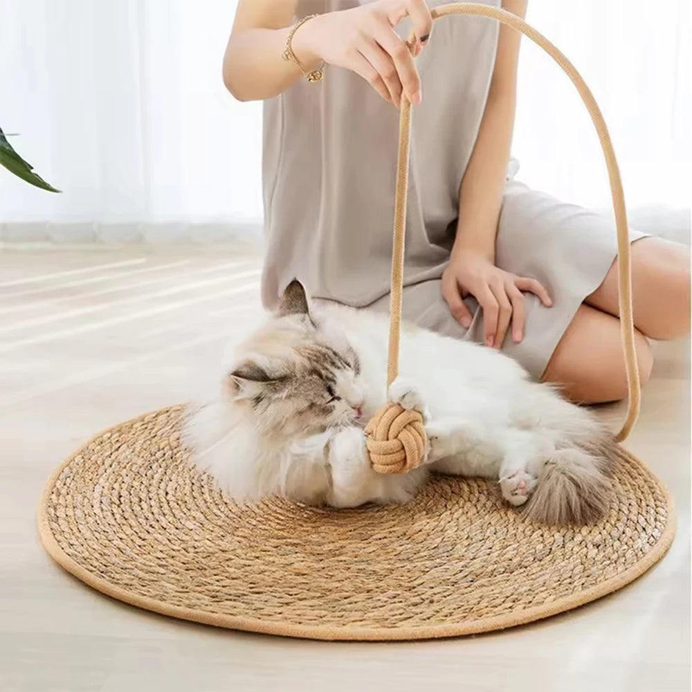 A white cat is relaxing on a round natural rattan mat, with a curved rattan stick nearby.