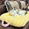 A fluffy brown and white cat is relaxing on a yellow plush oval pet bed.