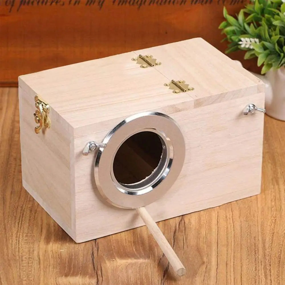 A light wood bird nesting box with a circular entrance and brass hardware sits on a wooden surface.