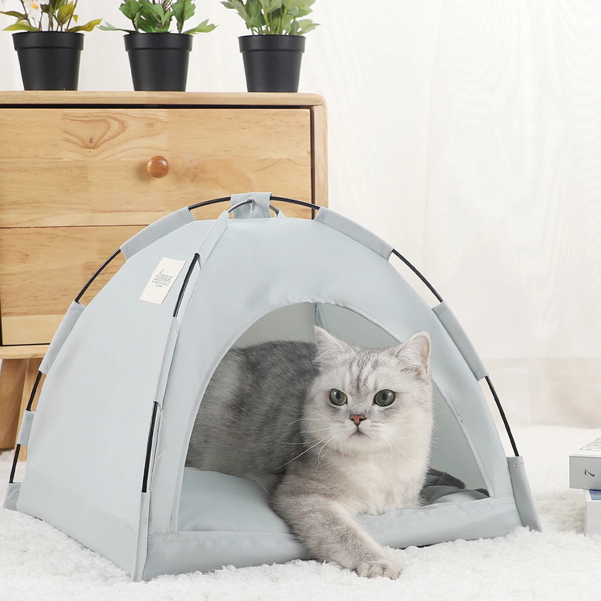 Un lit de tente pour chat bleu clair avec ouverture en maille sur un tapis blanc.