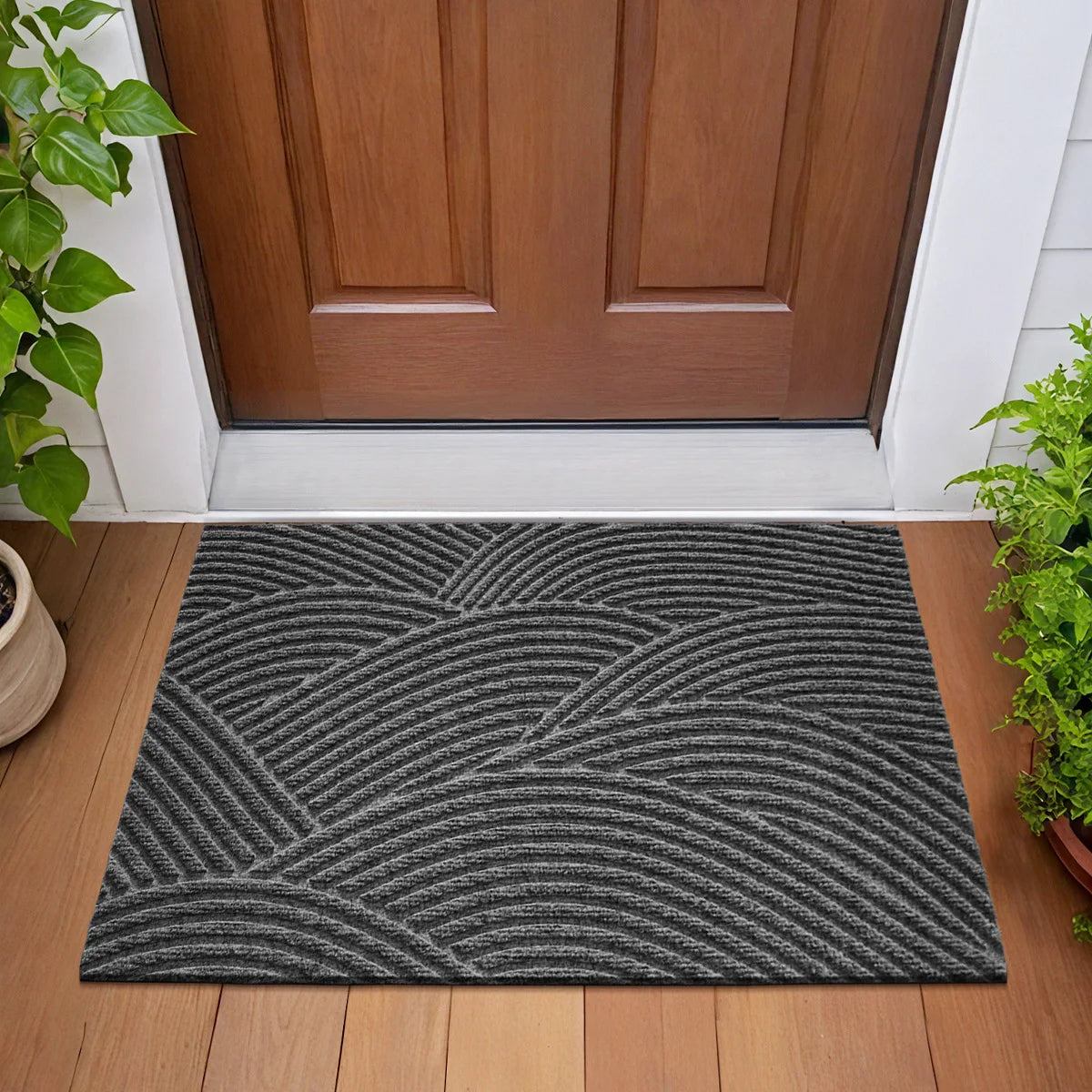 A rectangular gray geometric non-slip doormat placed on a wooden floor in front of a brown door.