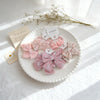 Présentation de nœuds pour cheveux élastiques roses et floraux avec des accessoires, disposés sur une assiette blanche avec d