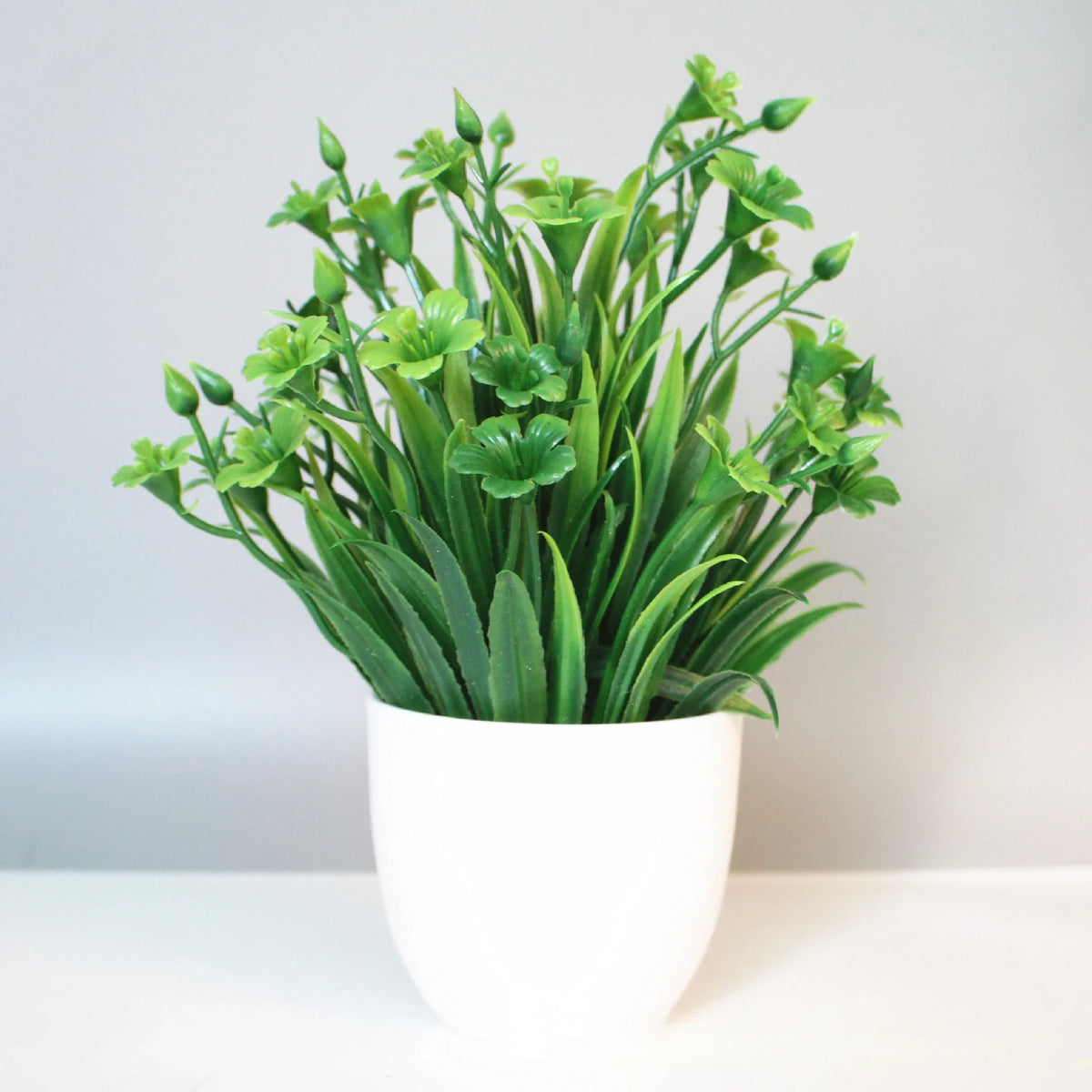 A potted artificial bonsai plant with bright green leaves displayed on a white surface.