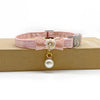 Pink lace flower cat collar with a pearl bell attached, resting on a brown box.