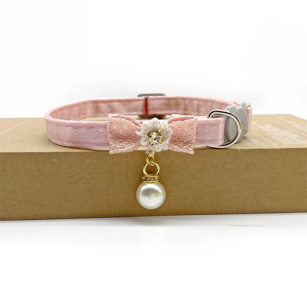 Pink lace flower cat collar with a pearl bell attached, resting on a brown box.