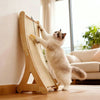 Un gato blanco peludo usa un rascador vertical de sisal natural para jugar en interiores sobre un suelo de madera.