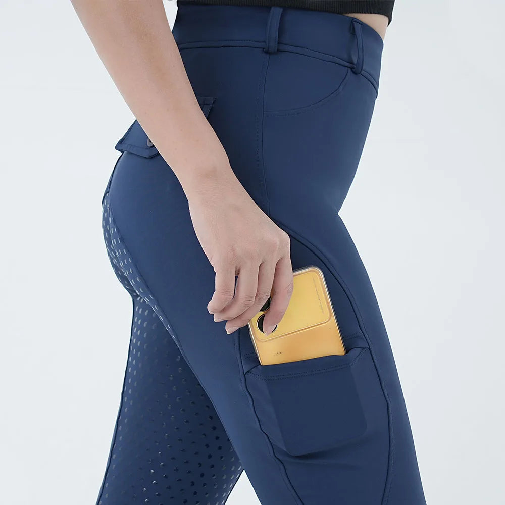 A close-up of a woman's hand adjusting a yellow pocket on dark blue women's full-seat riding breeches.