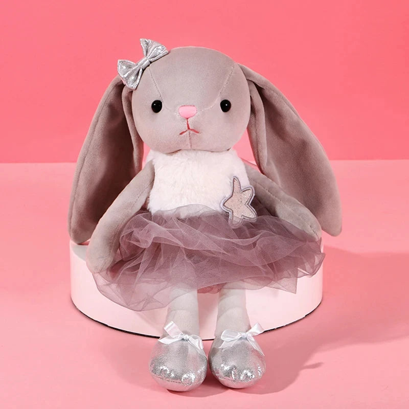 A soft gray plush rabbit toy with large floppy ears and a sheer tulle skirt, set against a pink background.