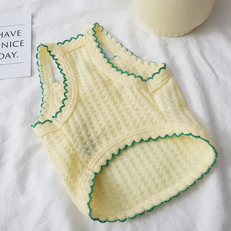 A yellow summer pet vest with green embroidery is displayed on a white towel.