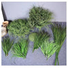A collection of green simulated onion grass used as garden decoration, displayed on a gray surface.