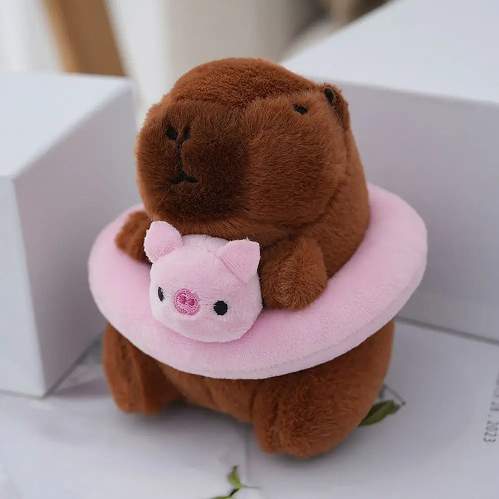 Braune Capybara-Plüschpuppe mit rosa Hoodie und kleinen Flügeln, in einer weißen Box saß.